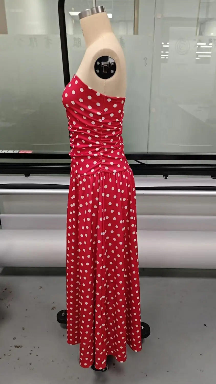 A vibrant red polka dot off shoulder strapless maxi dress made of flowing fabric that drapes elegantly.