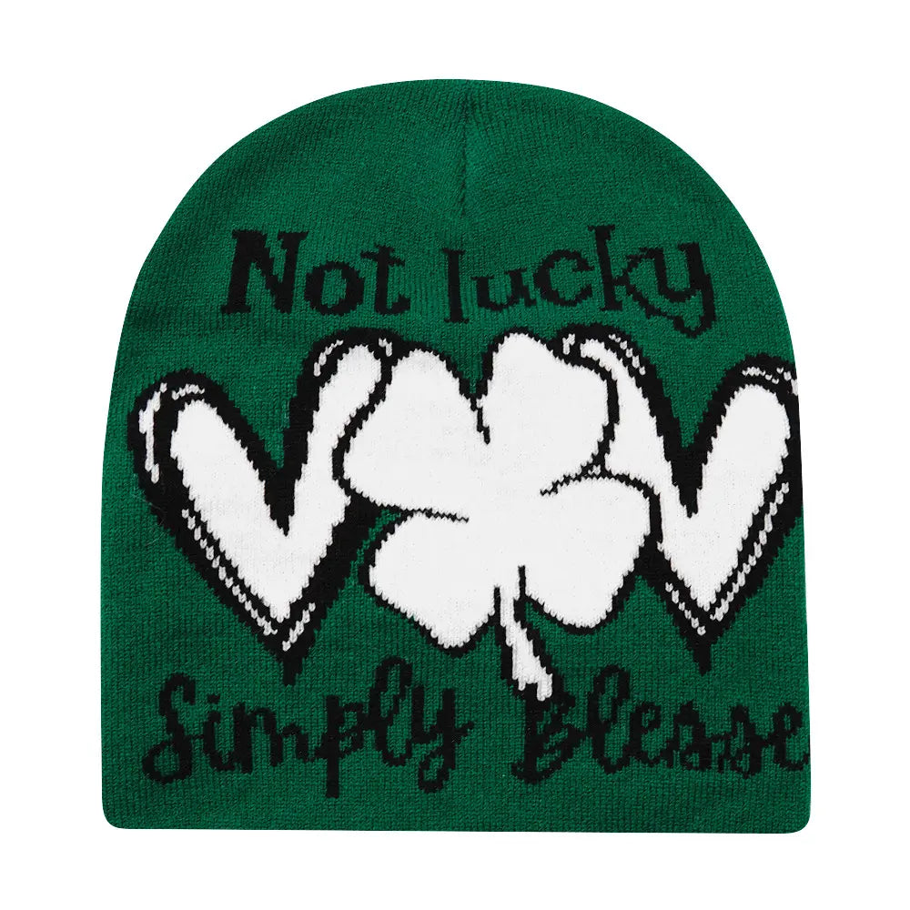 Green knitted beanie winter warm hat featuring a white shamrock with black outline and black script text not lucky above and simply blessed below.