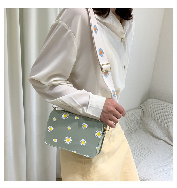 A light green pu leather daisy flower crossbody bag with a glossy finish and a chain strap featuring white daisy patterns and a matching strap adorned with small blue and orange flowers.