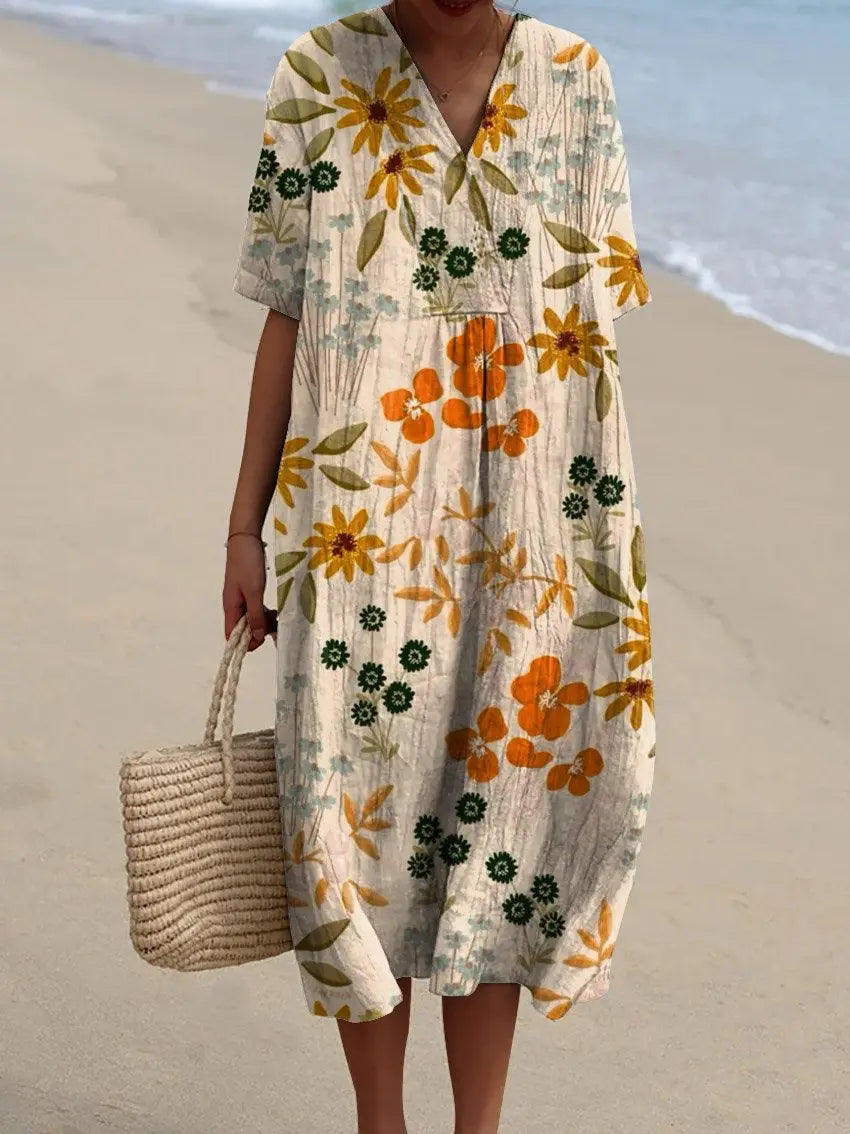 A flowing off-white short sleeve maxi dress with a vibrant floral print featuring orange and yellow sunflowers green leaves and small dark flowers on textured fabric.