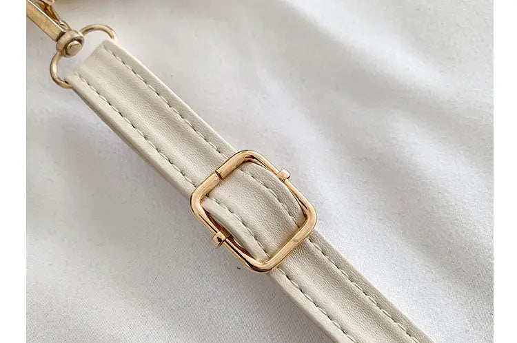 cream-colored faux leather strap with gold-tone metal buckle and hardware on quilted heart clasp crossbody bag with ruched handle