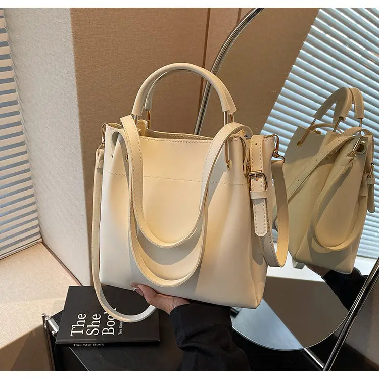 Cream-colored minimalist leather bucket bag with top handle and detachable shoulder strap.