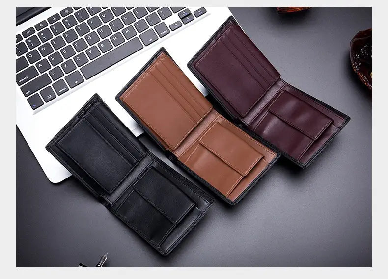 three men’s genuine leather bifold wallets in black brown and burgundy displayed open on a dark surface next to a laptop featuring a coin pocket.