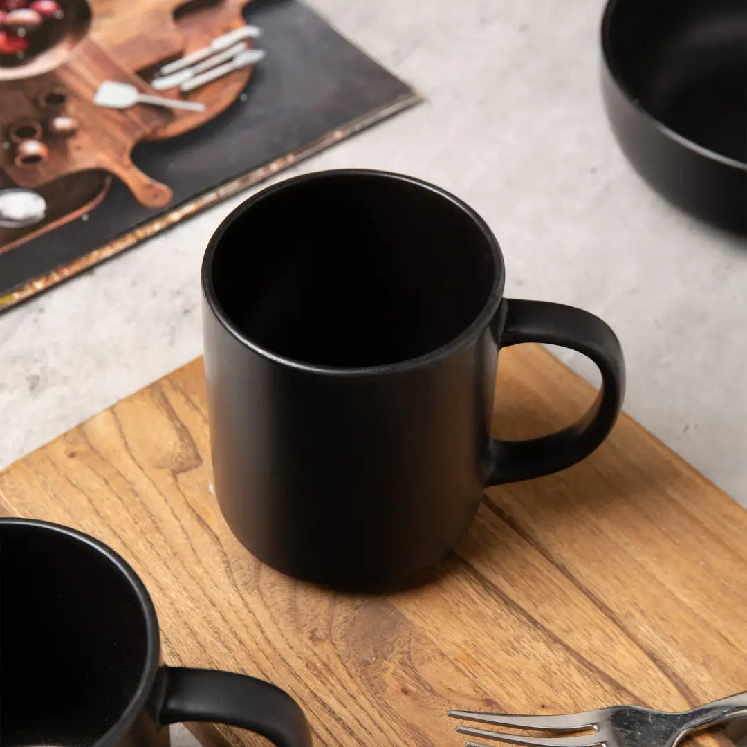 Taza de cerámica negra con acabado mate liso y forma cilíndrica sencilla, de un juego de vajilla de gres mate negro de 12 piezas para tres.