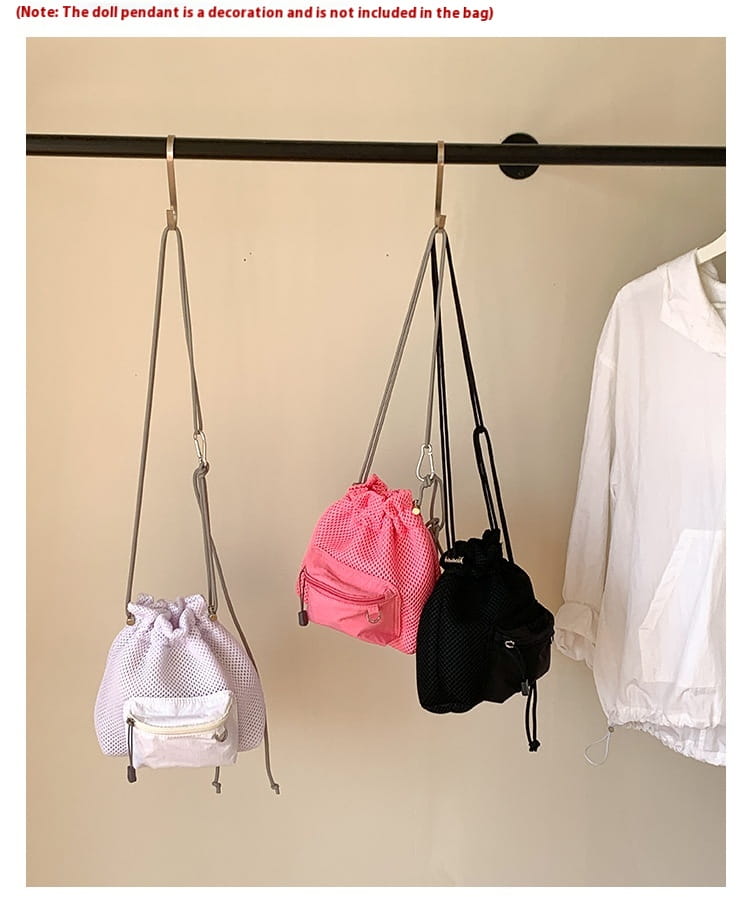three mesh drawstring mini backpacks in white pink and black hanging from a rod featuring the mini pink mesh drawstring bucket bag with heart charm