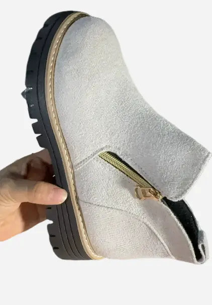 Botín de ante gris claro con suela negra de goma gruesa y detalle de cremallera lateral dorada.