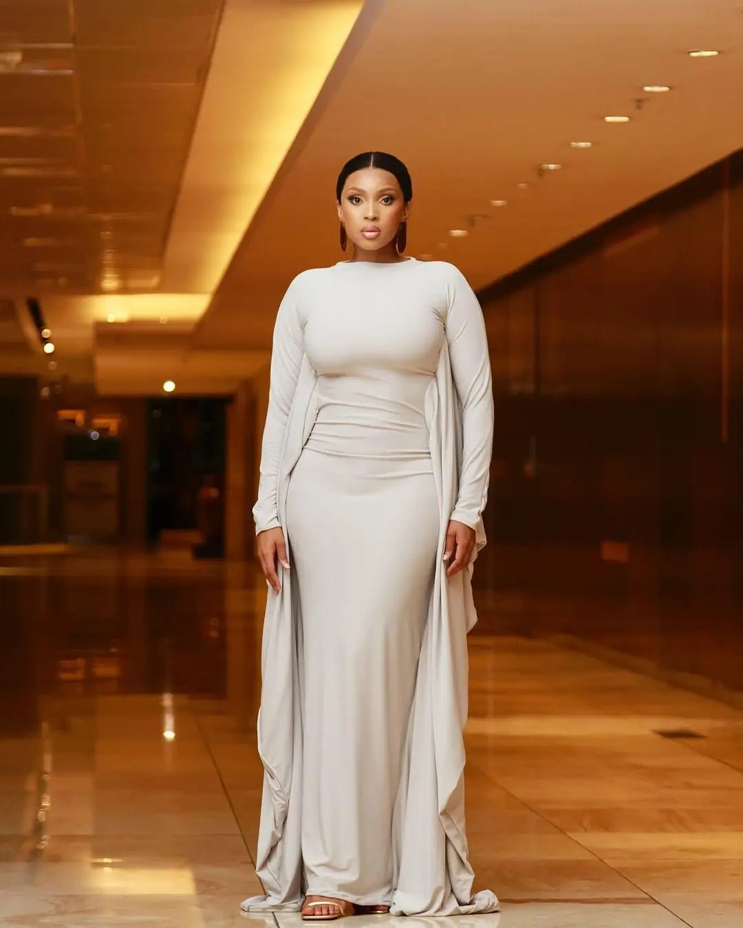 An off-white satin asymmetrical batwing sleeve maxi dress featuring a sleek fitted bodice and flowing cape-like sleeves.
