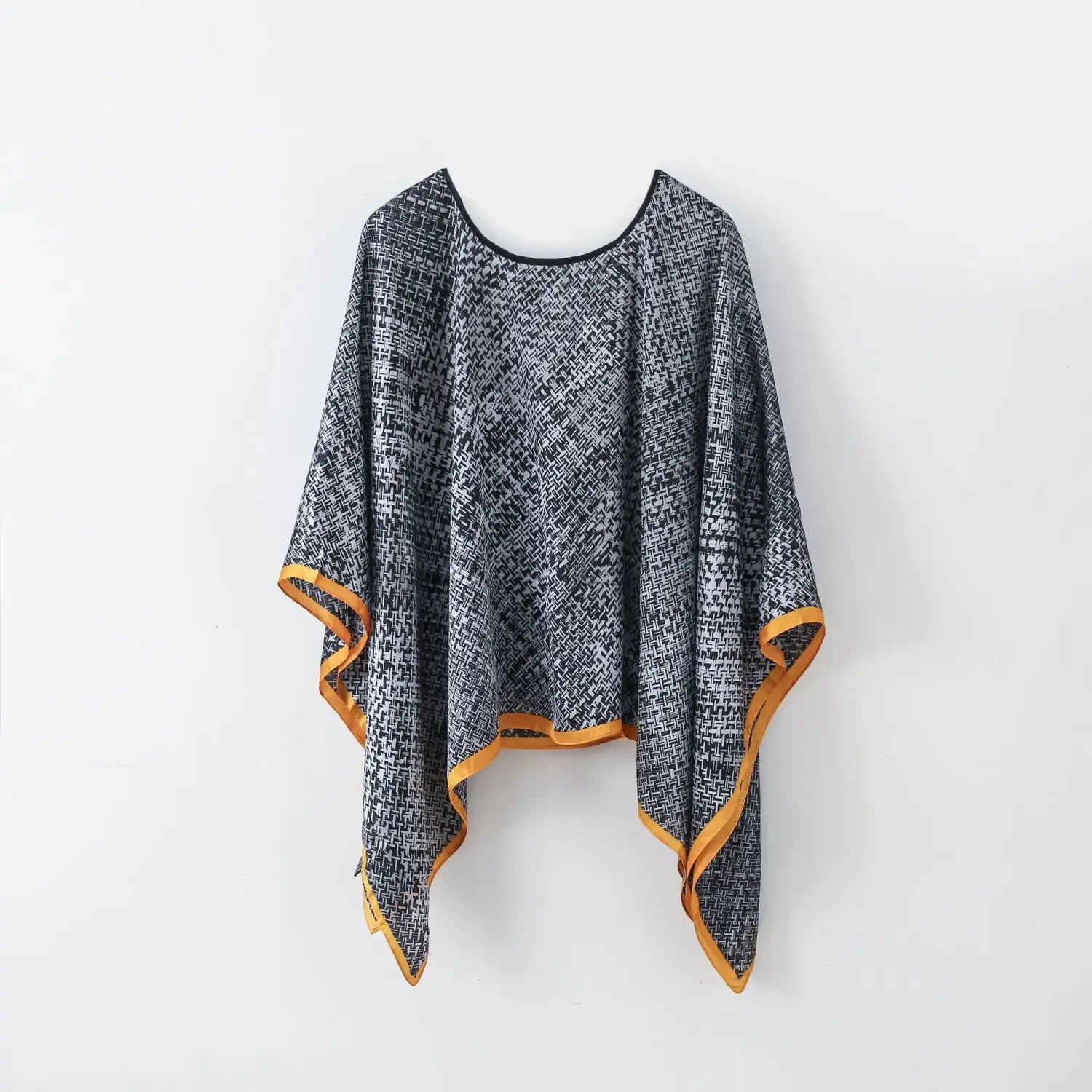 Printed silk patterned pullover shawl cape outerwear featuring a black and white poncho design with a contrasting mustard yellow trim along the edges.
