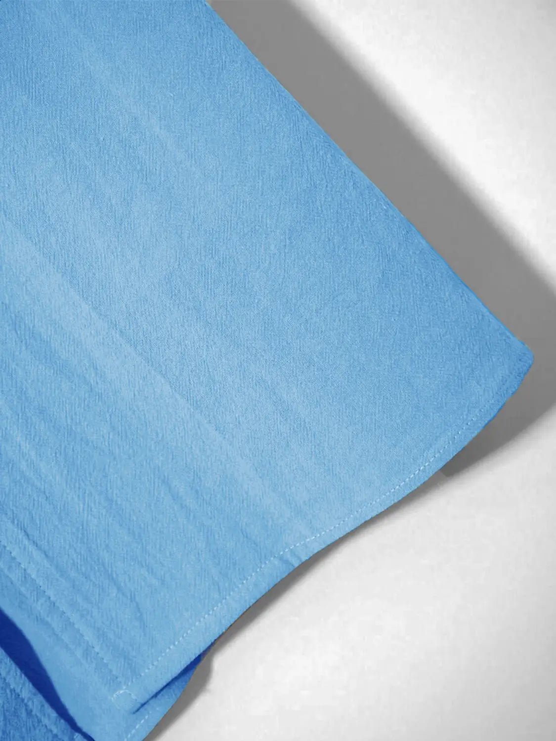 chemise en lin bleu clair boutonnée, confectionnée dans un tissu légèrement texturé, avec une couture verticale subtile le long du bord, pour un haut ample et décontracté pour homme.