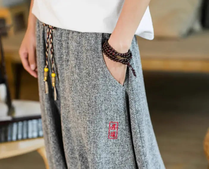 Herren-Shorts aus grauem bedrucktem Baumwollstoff im Lantern-Harem-Look mit weitem Bein mit quadratischem roten besticktem Patch auf der Seitennaht und geflochtenen Kordeln mit gelben Perlen.