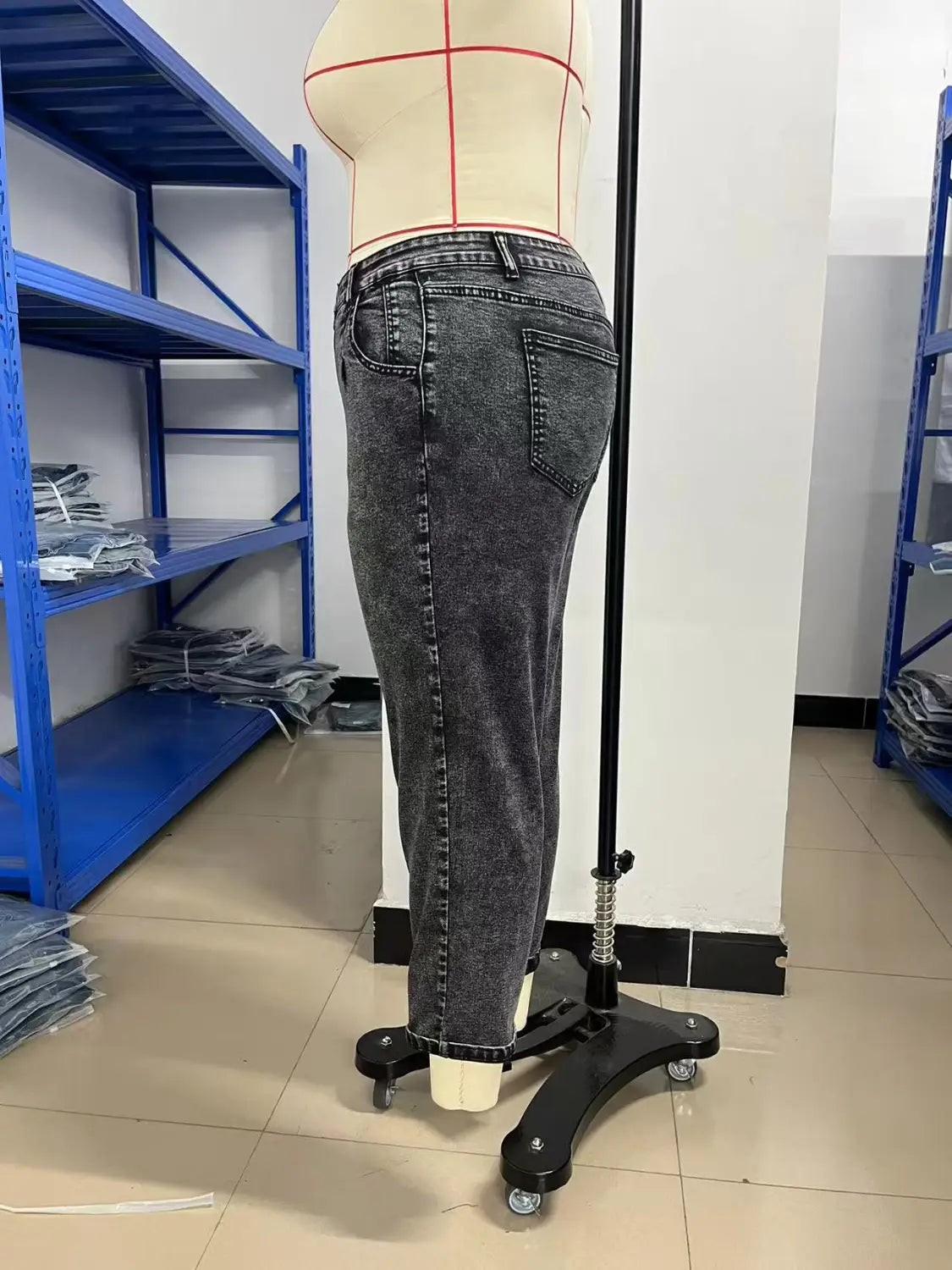 plus size retro washed tapered denim jeans in dark gray with a slightly faded wash and classic five-pocket design displayed on a mannequin in a garment workshop.