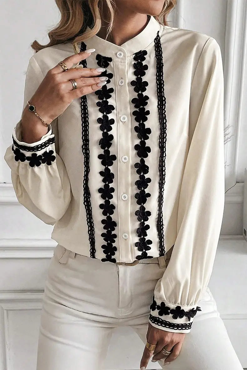 Cream-colored long-sleeved blouse featuring black floral embroidery and lace trim along the front placket, cuffs, and collar.