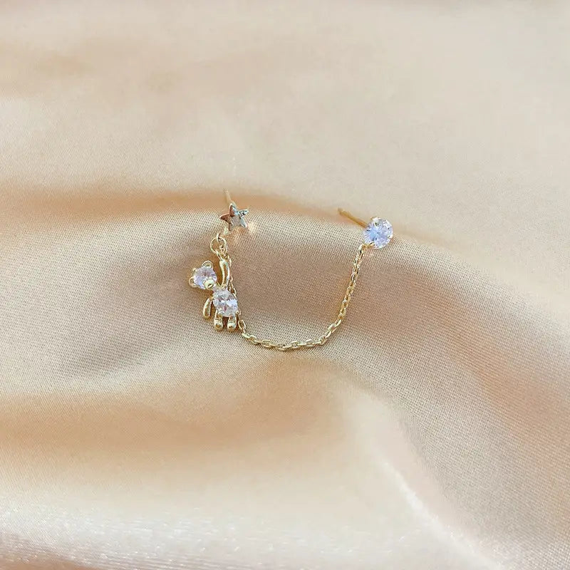 Boucle d’oreille à chaîne à finition dorée avec une petite breloque en forme d’ours et des accents en cristal transparent, provenant des boucles d’oreilles asymétriques en strass avec ours et pampilles étoilées.