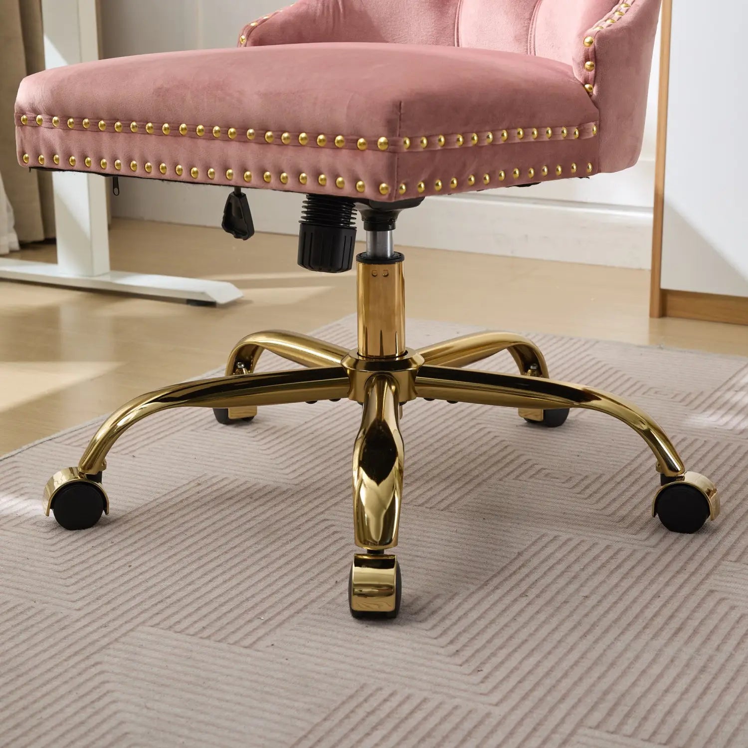 Fauteuil de bureau en velours rose poudré à capitonnage avec bordure à clous décoratifs ton doré et base en laiton poli, conçu pour un usage au bureau.