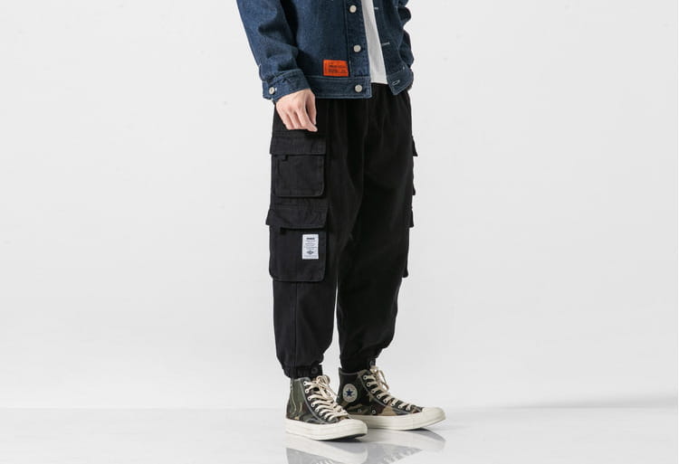 Pantalones cargo negros con múltiples bolsillos y cintura ajustable con cordón, diseñados como pantalones militares japoneses casuales de tiro cónico.