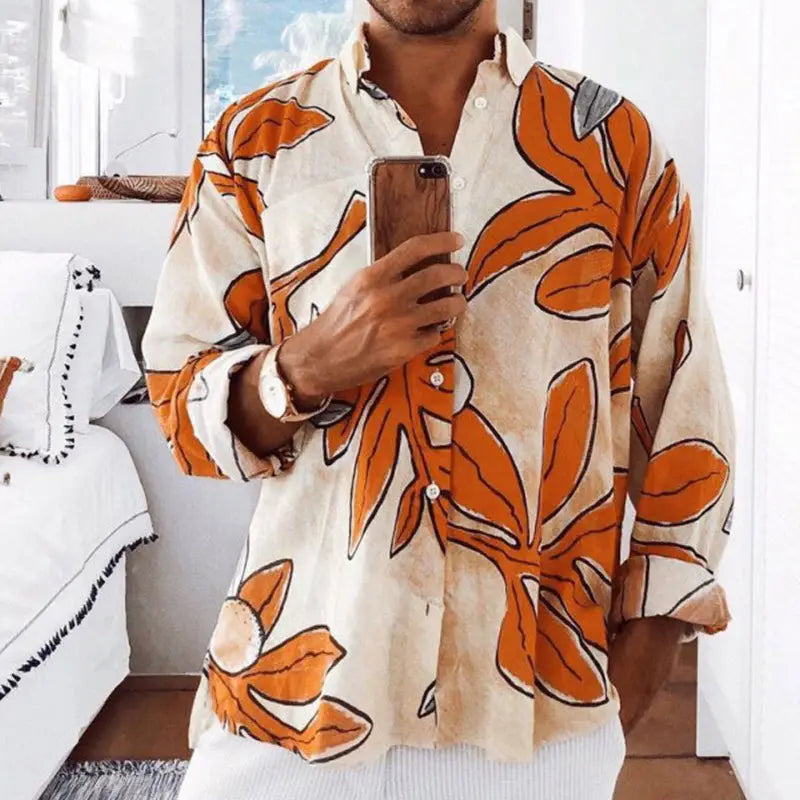 Ein Mann, der ein Hemd mit langem Ärmel und tropischem Print für Herren am Strand trägt, mit einem orangefarbenen Blattmuster auf einem cremefarbenen, locker sitzenden Stoff.