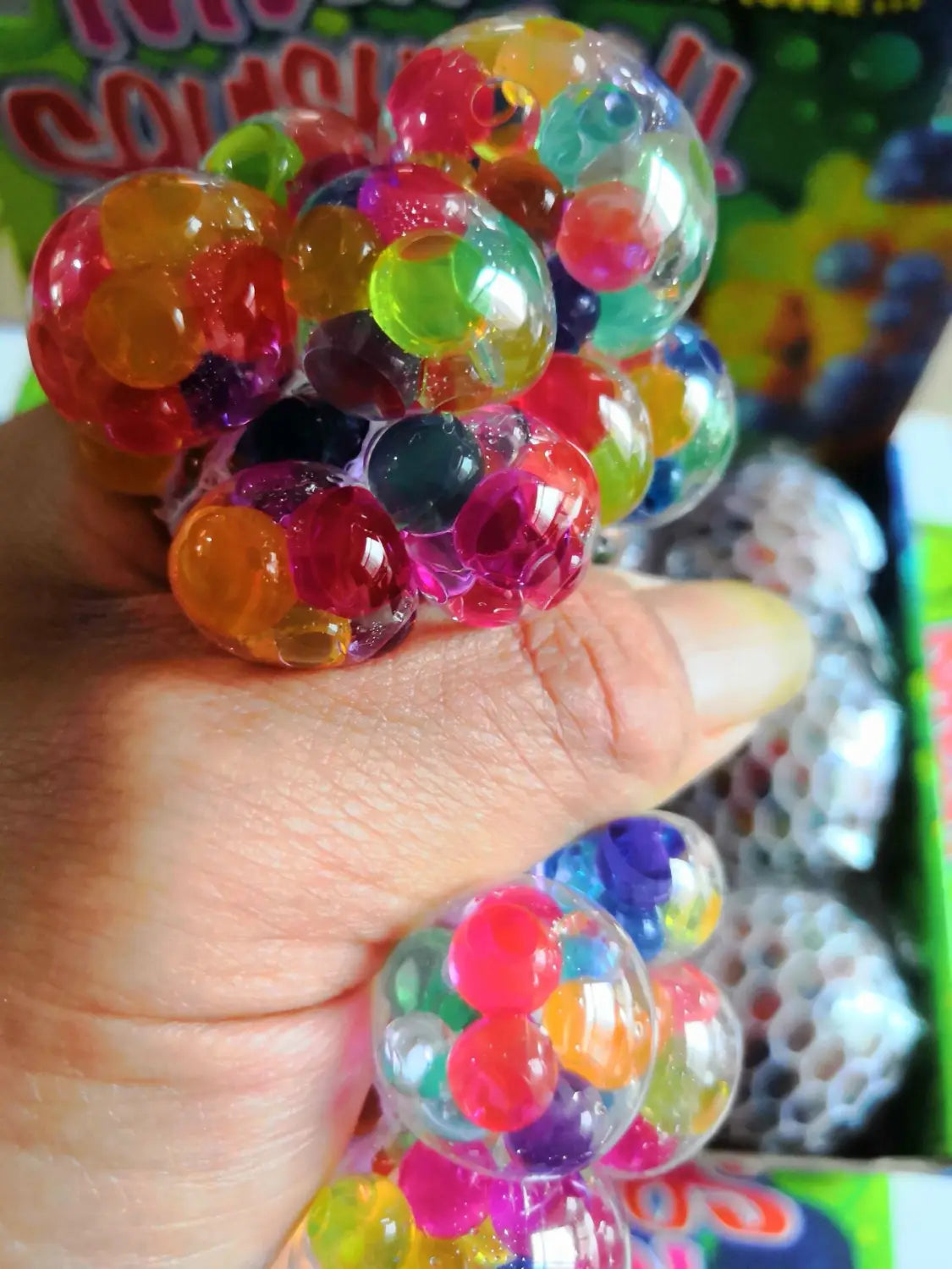A hand squeezes a colorful transparent LED mesh stress ball glowing grape squeeze toy filled with multicolored gel beads.