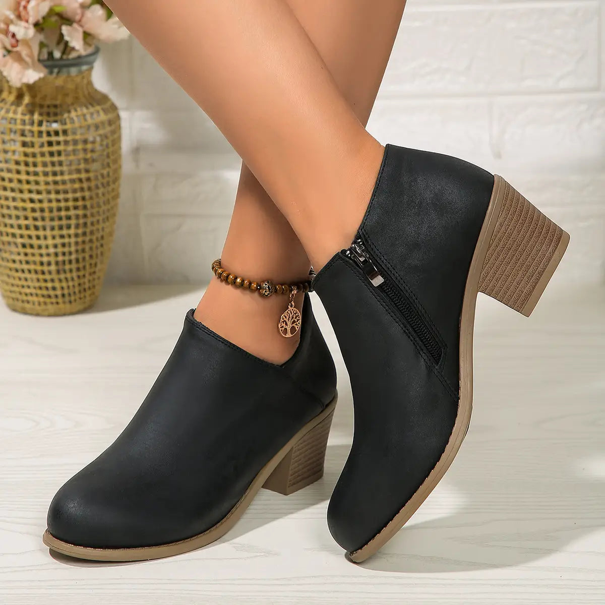 black leather ankle boots with chunky tan heel and side zipper closure shown from the back side