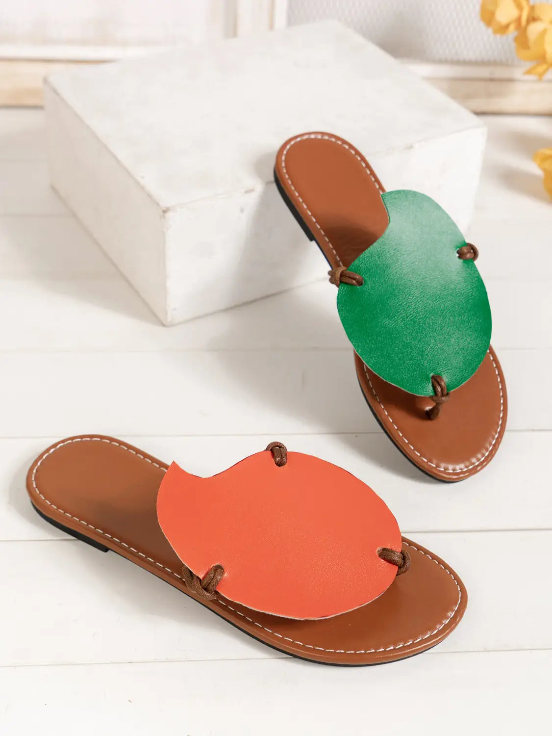 A pair of women’s brown leather slide sandals with vibrant green and orange circular leather accents designed for casual flat wear.