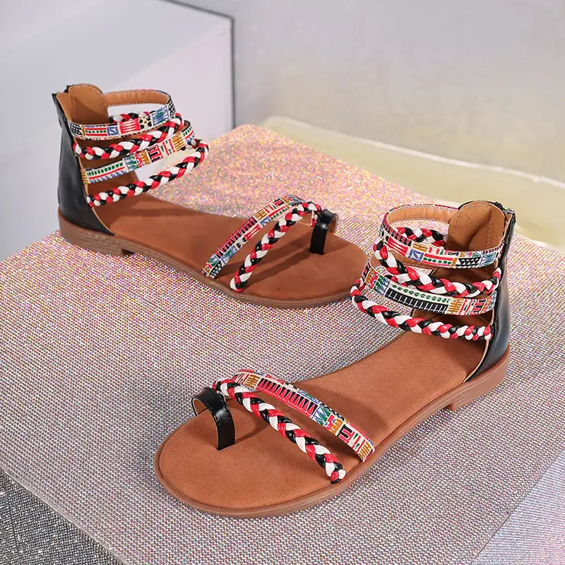 Black and tan strappy flat sandals with colorful braided ankle straps featuring bohemian ethnic geometric patterns.