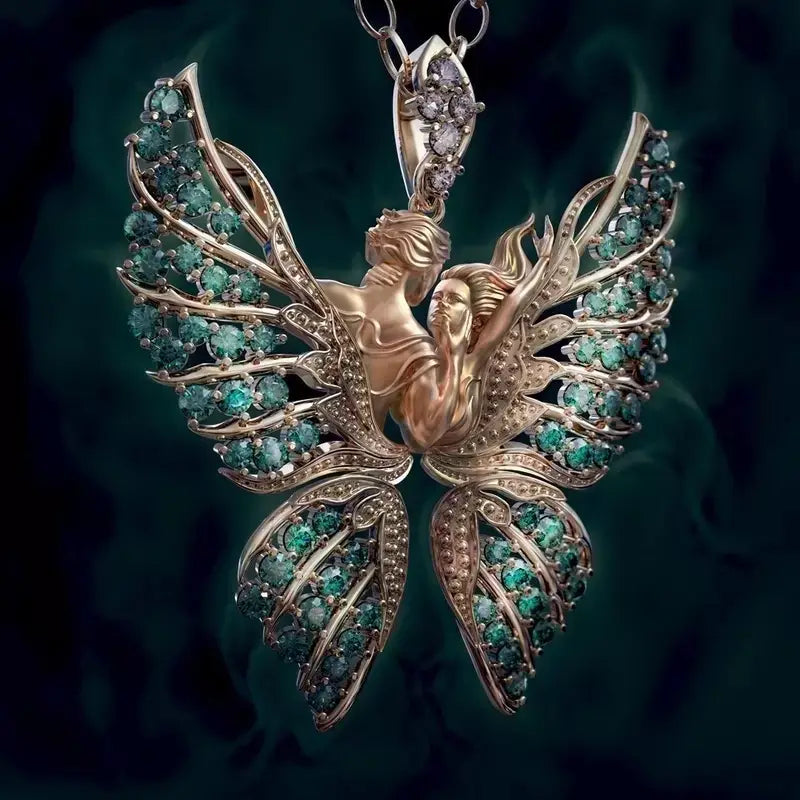 A delicate gold pendant necklace featuring two intertwined figures with expansive angel wings adorned with vibrant green emerald stones and sparkling diamonds.