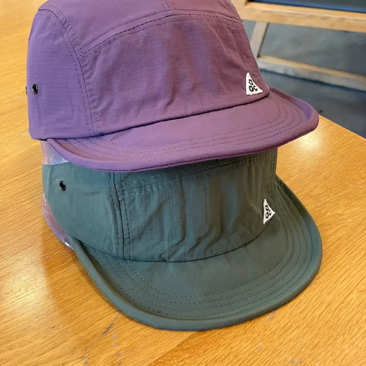 Quick drying short brim cap featuring purple and olive green Nike ACG five-panel hats with a subtle textured fabric finish.