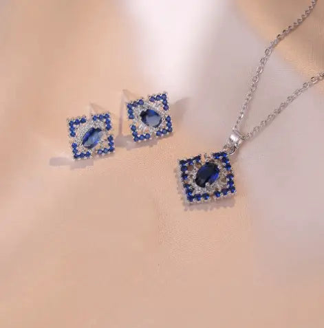Blue and silver square pendant necklace featuring a central oval blue zircon gemstone surrounded by smaller clear stones on a titanium chain from the elegant blue zircon flower jewelry set.