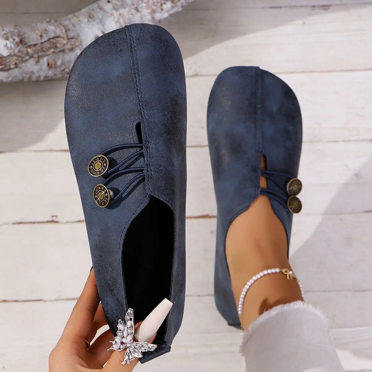 navy blue suede slip-on women’s loafers featuring gold-tone button accents and a butterfly charm at the heel with a square toe and lace-up leather detailing.