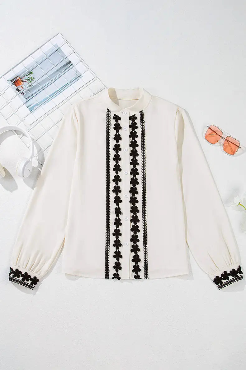 Cream-colored long-sleeved blouse featuring black floral embroidery along the front placket and cuffs with lace trim.
