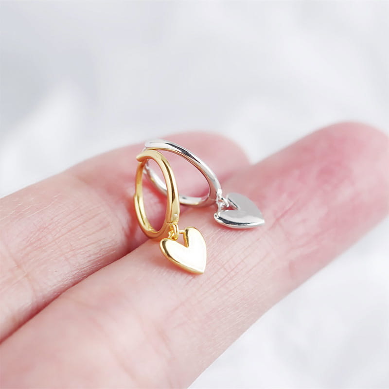 Minimalistische herzförmige Creolen aus Gold und Silber, auf einer Fingerspitze platziert, mit ihrem Anhänger-Design.