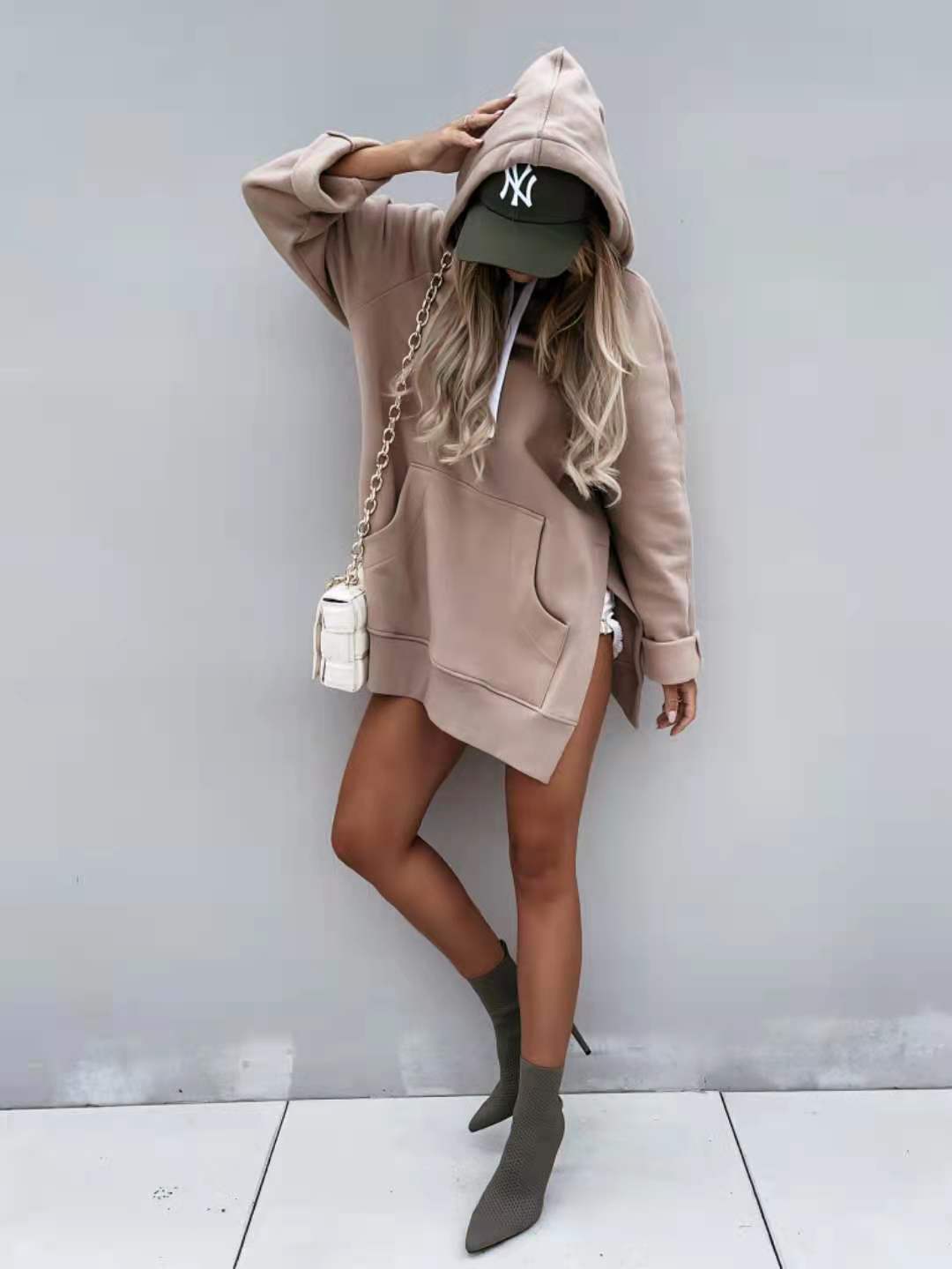 beige oversized mid length hooded sweatshirt dress with front pockets and drawstring hood worn over a green baseball cap