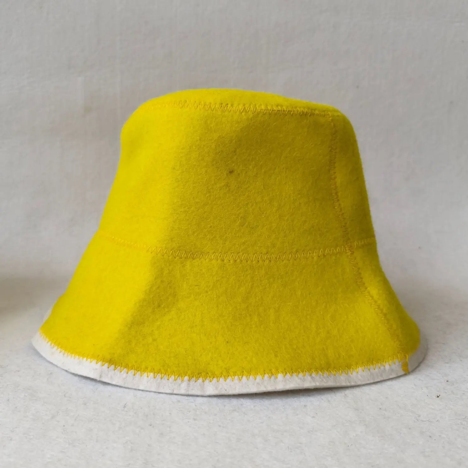 Eine kräftige gelbe Wollfilz-Fischerhut-Kappe mit kontrastierendem weißem, aufgesticktem Zierbesatz entlang des Randes, geeignet für die Winterkleidung.