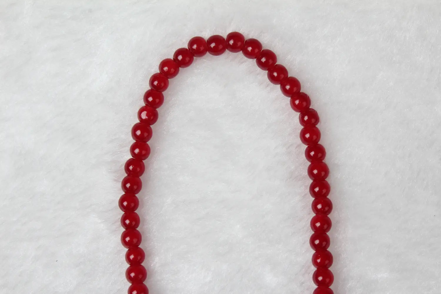 A red agate good luck bracelet featuring vibrant red faceted glass beads arranged in a gentle curve with an engraved protect charm.