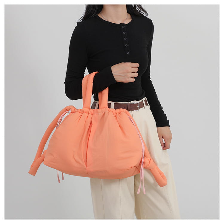 A soft peach-colored quilted puffer tote bag made of lightweight nylon with drawstring closure and matching handles.