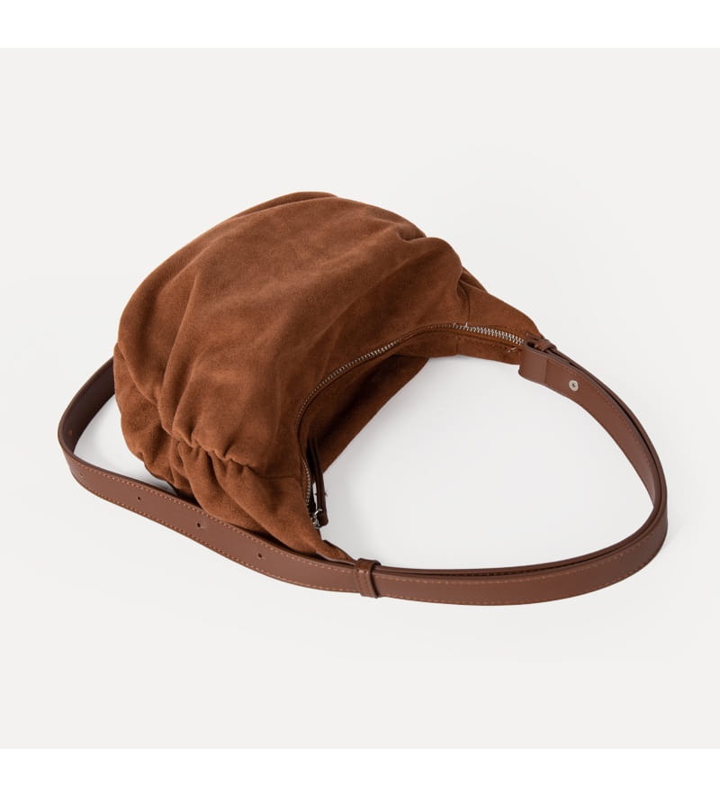 Brown suede dumpling shoulder bag with slouchy crossbody design, matching leather strap, and zipper closure.