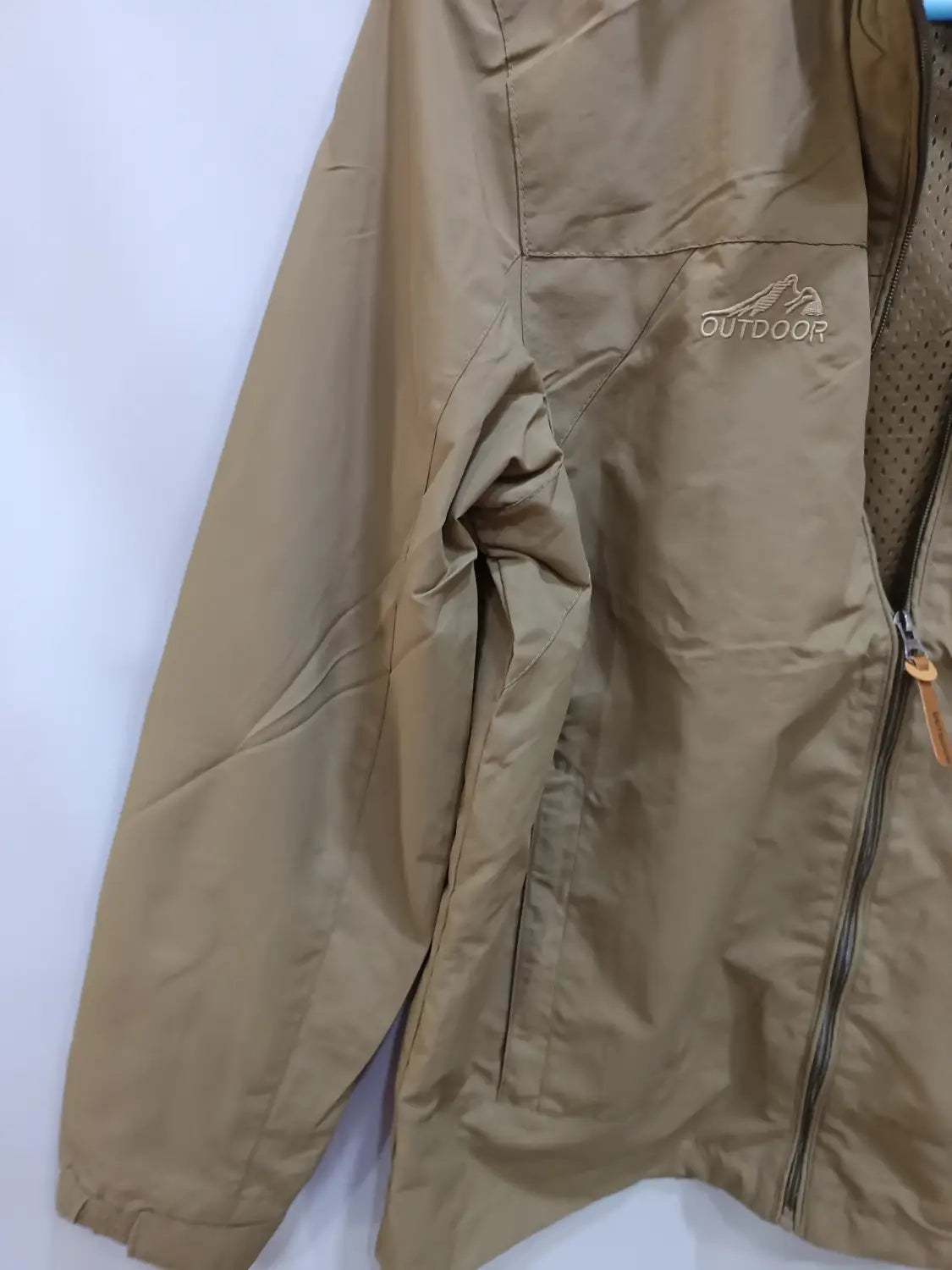 Chaqueta de senderismo con capucha impermeable color camel, con un logotipo exterior bordado sutil en el pecho y un tirador de cremallera naranja.