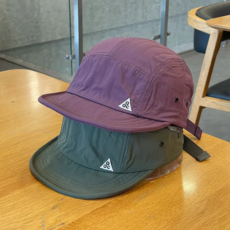 Purple and olive green quick drying five panel cap with a short brim and a white triangular logo on the front.