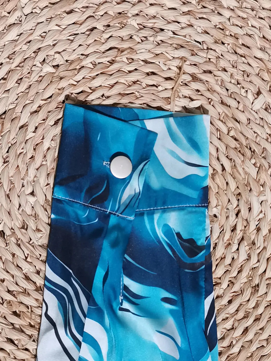 a blue and white abstract patterned fabric pouch with a silver button closure paired with a women’s marble print satin long sleeve button blouse