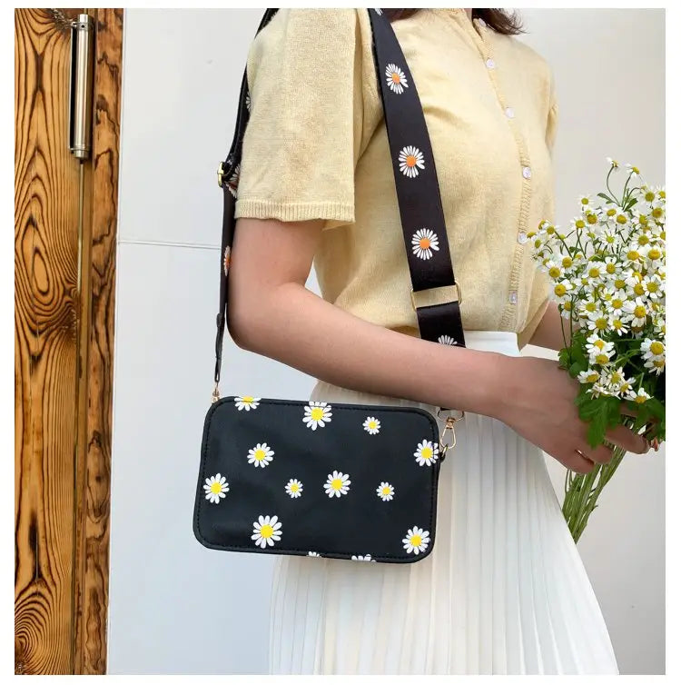 Black crossbody pu leather bag with white and yellow daisy flower pattern and chain strap.