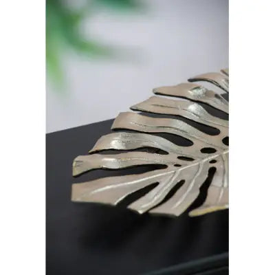 Silver-toned metal monstera leaf decorative piece with cut-out vein patterns featured in gold monstera leaf wall decor and serving tray.