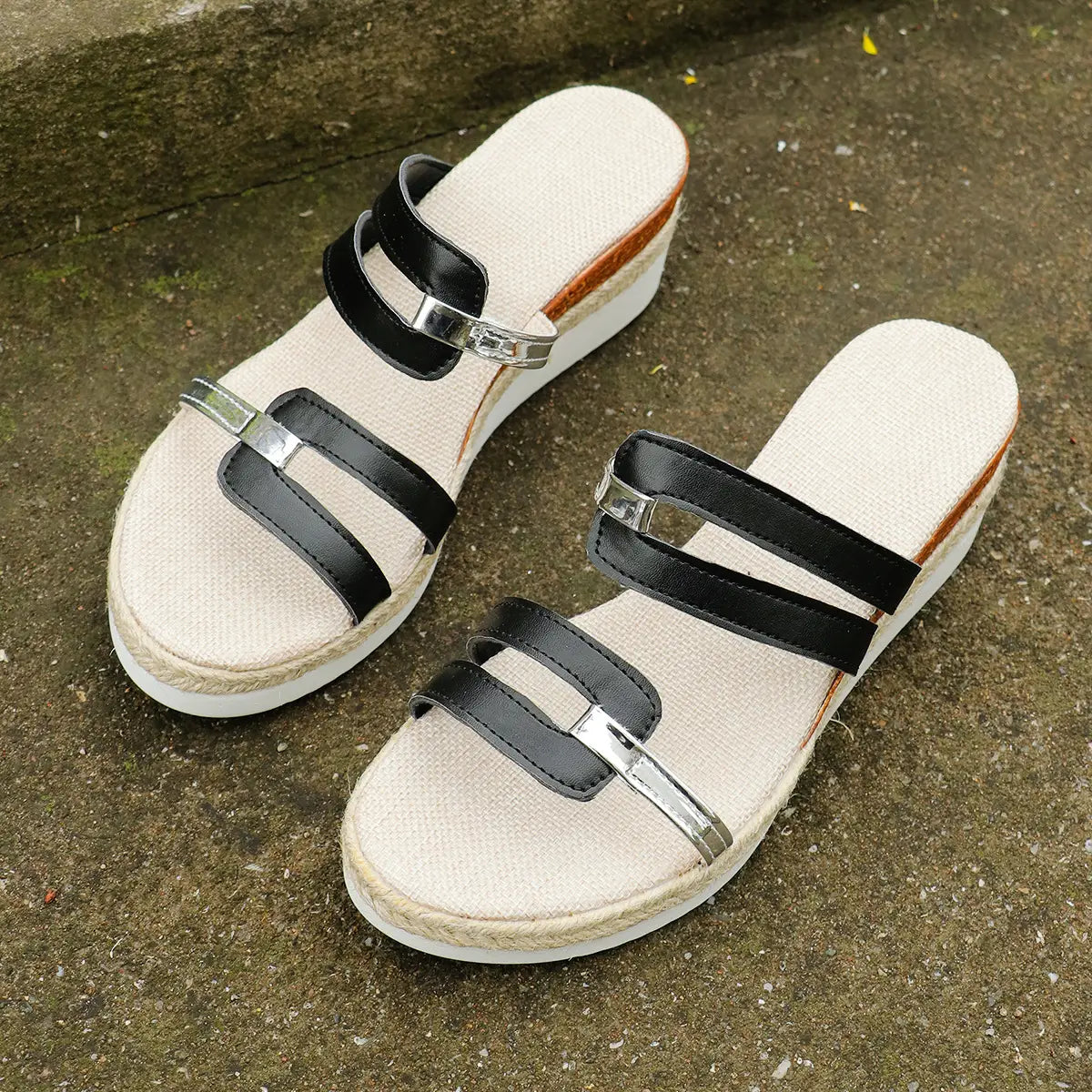Black and beige wedge sandals with espadrille heel and silver buckle metal accents displayed from the back side