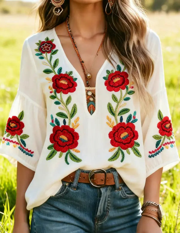 Weiße bestickte Bluse mit kräftigen roten Floralmotiven und grünen Blättern, mit farbigen Akzenten in einem böhmischen, floral bestickten Blusendesign.