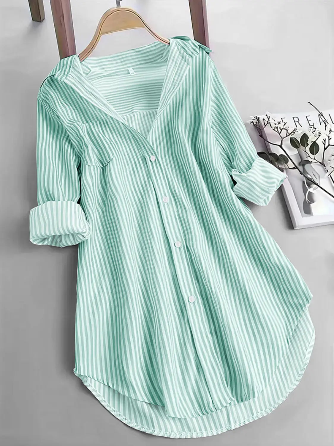 Chemise boutonnée à manches longues à rayures verticales vert clair et blanches, poignets retroussés, suspendue à un cintre en bois, idéale pour un usage décontracté.