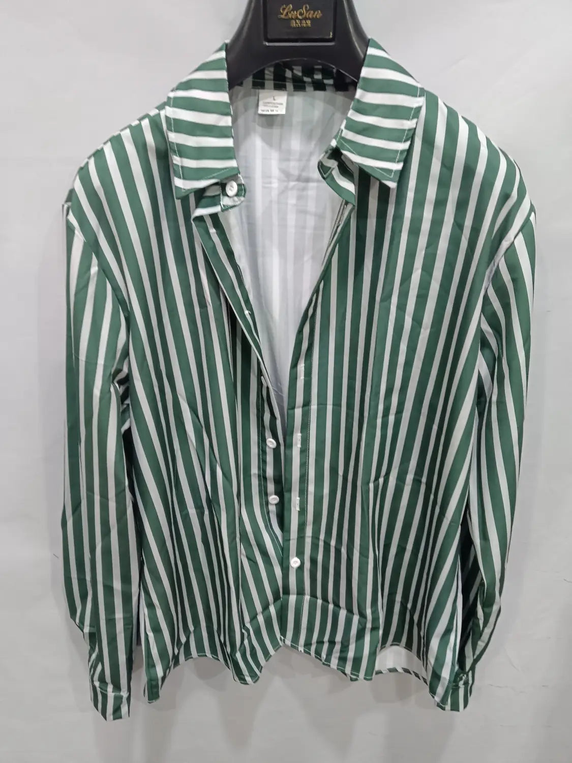 Chemise décontractée à manches longues rayée verticalement vert et blanc pour hommes, avec col classique, suspendue sur un cintre noir.