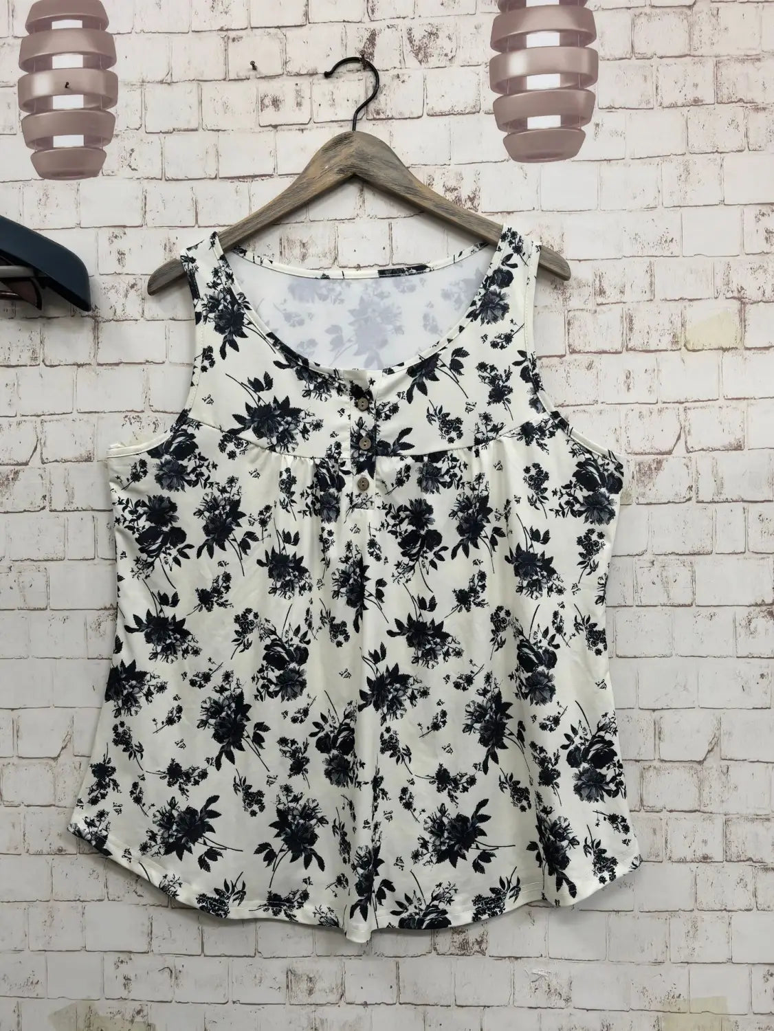 木製ハンガーに掛けられた、黒と白の花柄プリントのノースリーブニットキャミソールで、ボタン前のディテール付き。