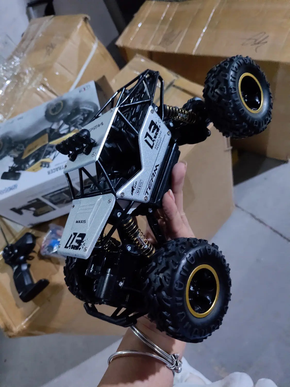 Camion teledirigido RC todoterreno 4WD de alta velocidad en negro y blanco, tipo crawler, con neumáticos con aros dorados y un diseño de chasis resistente.