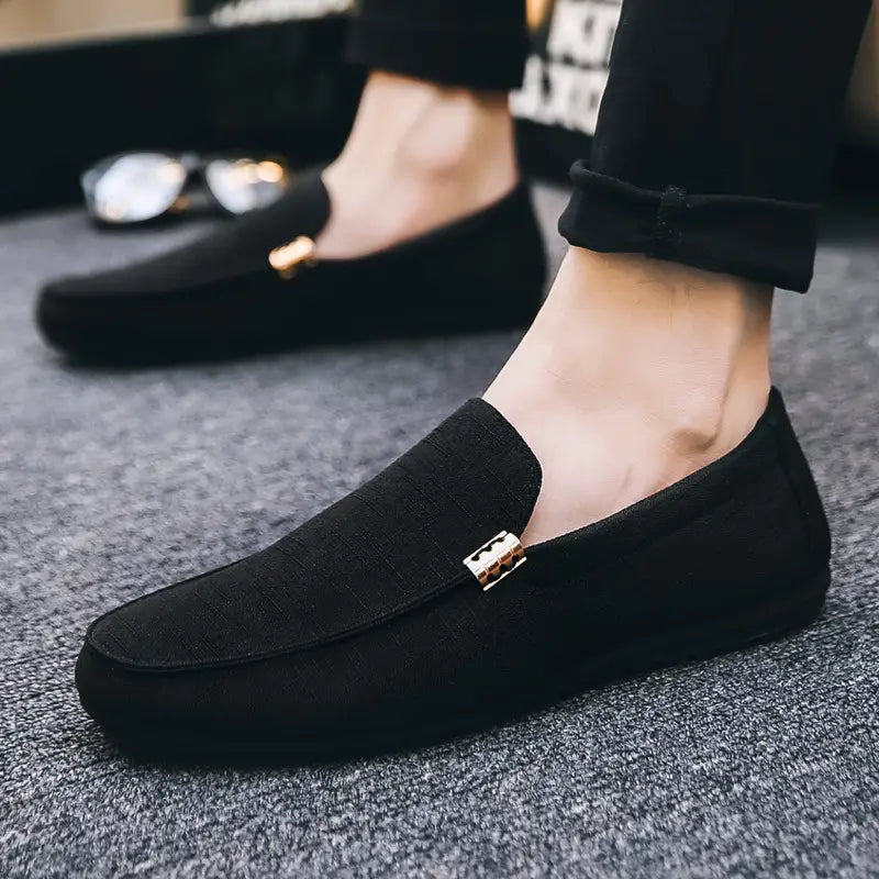 Mocassins en daim noir pour homme avec détail de boucle rectangulaire ton or, conçus comme des chaussures à enfiler.