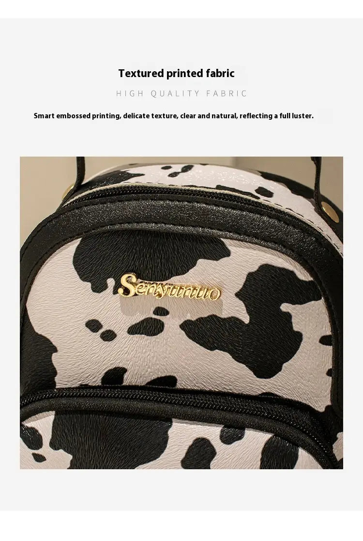 Mini backpack featuring black and white cow print with gold-tone sensyinuo logo embroidery in Korean style.