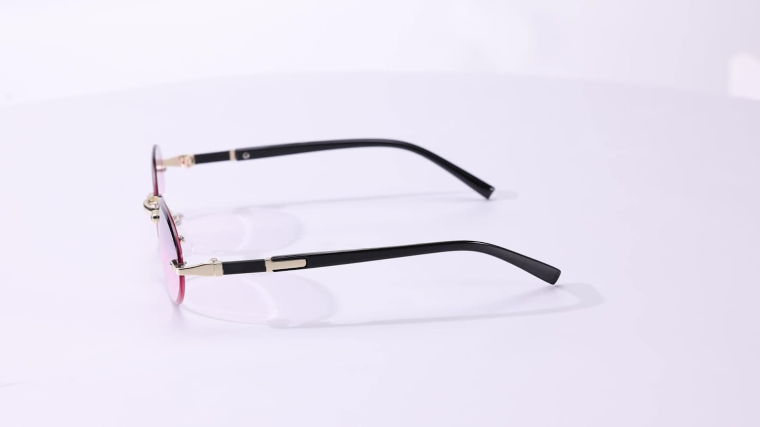Frameless oval uv400 fashion sunglasses with black frames pink-tinted lenses and gold-tone metal accents.