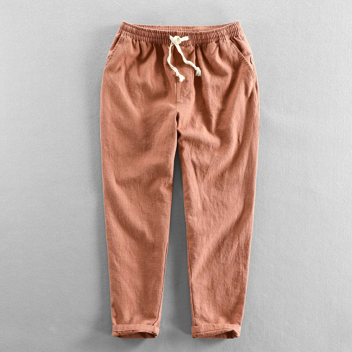 men’s relaxed fit drawstring linen joggers in muted terracotta cotton twill with an elastic waistband and cream-colored drawstrings.